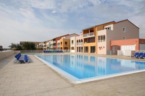 une grande piscine avec des chaises bleues et des bâtiments dans l'établissement Appartement superbe vue -Climatisation - piscine - parking - 5MC317, au Barcarès