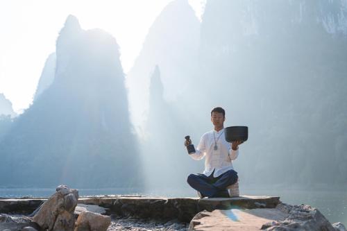 a man sitting on a rock in front of a waterfall at Leisure Courtyard Hotel Yangshuo in Yangshuo