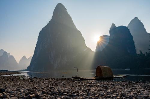 a boat on a rocky beach with mountains in the background at Leisure Courtyard Hotel Yangshuo in Yangshuo