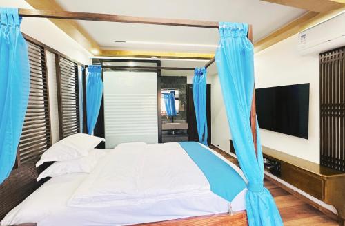 a bedroom with a bed with blue curtains and a tv at LQJ Riverside Guest House in Fenghuang