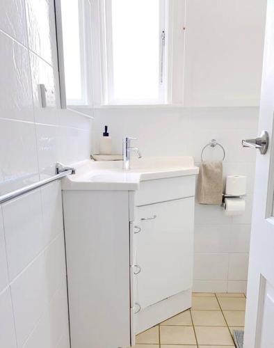 a white bathroom with a sink and a window at 3-Bedroom House near Train Station with Netflix in Revesby