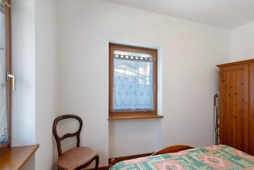 a bedroom with a bed and a chair and a window at Residence Malibu Appartamento 2 in Falcade
