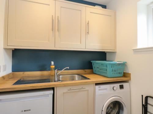 a kitchen with white cabinets and a sink and a dishwasher at Tirlaggan Úr in Oban