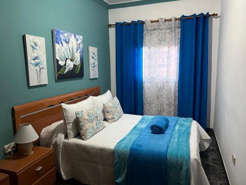 a bedroom with a bed and a window with blue curtains at La Casita de Omar en el corazón de Anaga y La Laguna in Las Mercedes