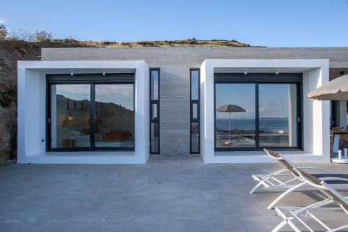 a house with glass doors and chairs on a patio at Magic Cave Villa in Tinos in Agios Sostis
