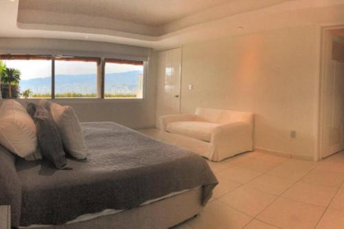 a bedroom with a bed and a chair and a window at Penthouse en Las Brisas Acapulco in Acapulco