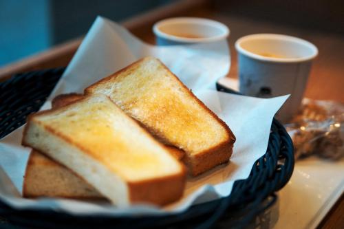 a basket with two slices of toast on a table with cups of coffee at Hotel Mermoz Paris Le Bourget in La Courneuve