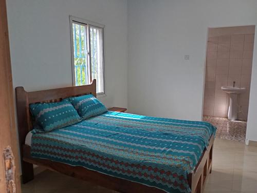 a bedroom with a bed with a blue comforter and a window at Baafeh Beach in Sanyang