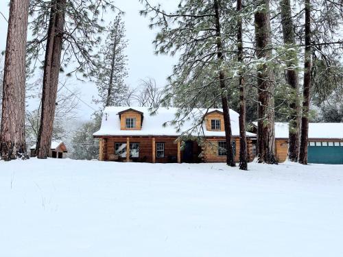 a log cabin in the snow with trees at Log Cabin w/ pool, spa, game room, sleeps 20 in Coarsegold