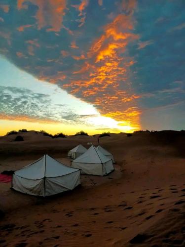 two tents on a beach with a sunset in the background at Sahara Camp Light in Mhamid