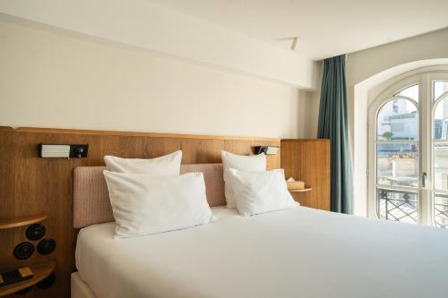 a bed with white pillows in a room with a window at Hôtel du Sentier in Paris