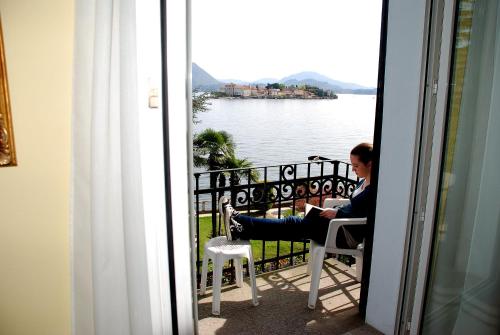 a woman sitting in a chair on a balcony looking at the water at Hotel Villa Ruscello in Baveno