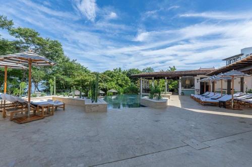 a patio with tables and umbrellas and a pool at Trendy Condo with Modern Decor, Stunning Ocean Views, and Exclusive Beach Club Access in Playa Danta