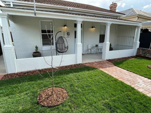 a white house with a tree in the yard at Baxter Cottage in Bendigo