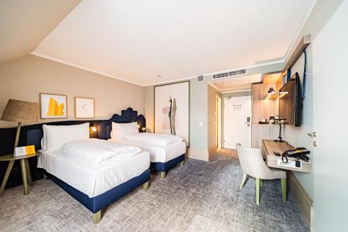 a hotel room with two beds and a desk at voco Vienna Prater by IHG in Vienna
