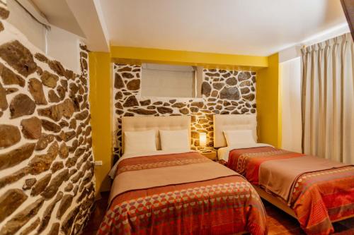two beds in a room with a stone wall at Kamma Guest House in Ollantaytambo