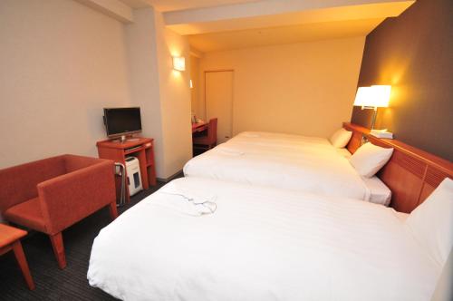 a hotel room with two beds and a chair at Hotel Premium Green Plus in Sendai