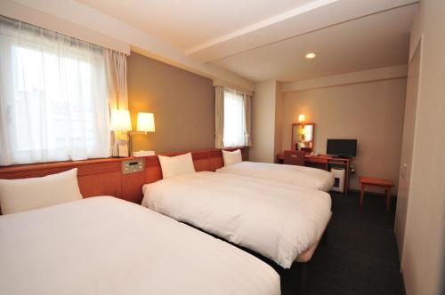 a hotel room with three beds and a desk at Hotel Premium Green Plus in Sendai