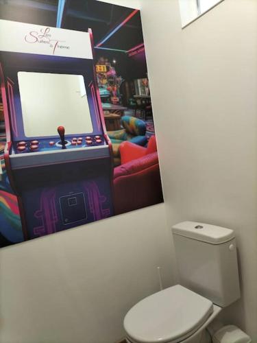 une photo d'une machine de jeux vidéo à côté de toilettes dans l'établissement La suite Gaming - Suite 8 personnes, à Rethel