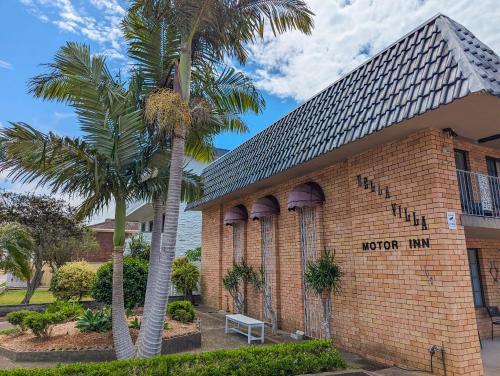 a brick building with palm trees in front of it at Bella Villa Motor Inn in Forster