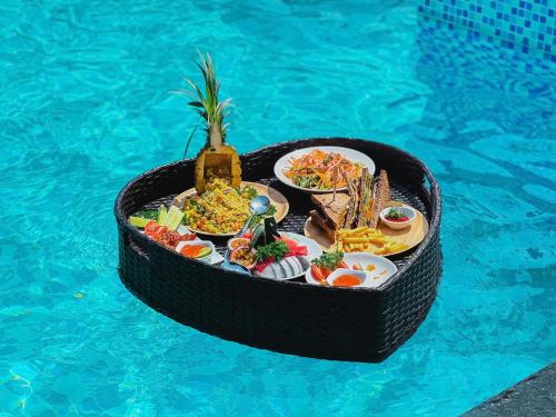 a table of food in a basket next to a swimming pool at The Sail Hotel - My Khe Beach in Da Nang