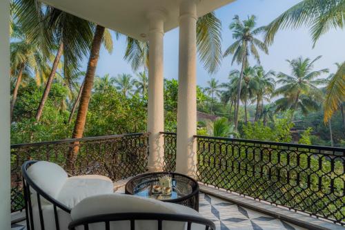 a balcony with chairs and a table and palm trees at ELIVAAS 4 BHK Villa with Pvt Pool & Jacuzzi-Yashgeet in Siolim