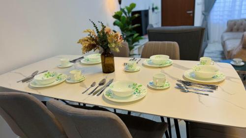 a table with plates and cups and a vase with flowers at KLIA Sepang Charming 4-Bedroom Blissful Double-Storey Home in Sepang
