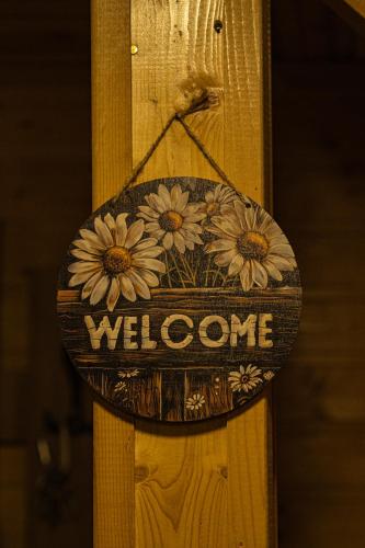 a welcome sign on a wooden pole with flowers on it at Wooden Villa Sormoni in Tskaltubo