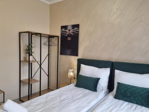 a bedroom with a bed with white sheets and green pillows at Dezudava Family Hotel in Sandanski