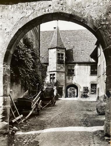 une photo en noir et blanc d'un bâtiment avec une arche dans l'établissement Domaine La Cour Des Nobles - Demeure, Maison et Appartements au coeur de Riquewihr, à Riquewihr