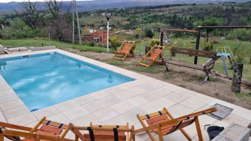 a swimming pool with two chairs and a playground at Terrazas al Champaqui in Villa Yacanto