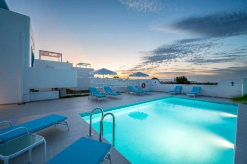 a large swimming pool with blue chairs and a sunset at XENOS VILLA 6 With a private pool near the sea in Tigaki