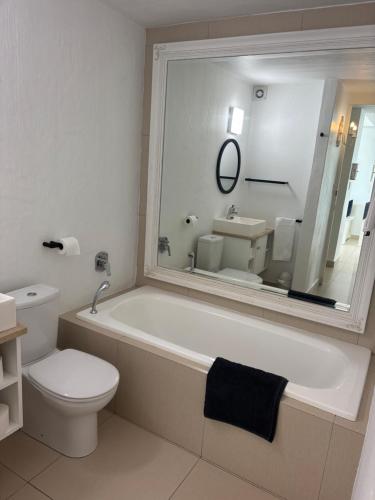 a bathroom with a tub and a toilet and a mirror at Palm Cove - 52 Chakas Cove, Penthouse-Literally on the Beach in Ballito