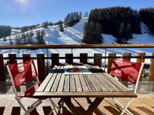 a wooden table and two chairs on a deck with snow at Deux pièces face aux pistes in Péone