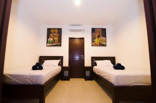 two beds in a room with paintings on the wall at Sanur Guest House in Sanur