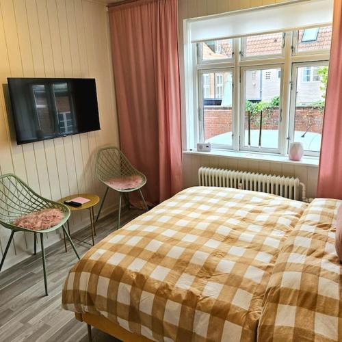 a bedroom with a bed and two chairs and a television at Idyllisk Mini-Hus i det charmerende Latinerkvarter in Viborg