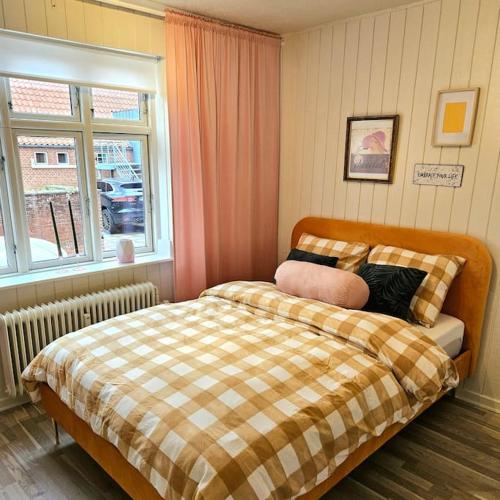 a bedroom with a bed with a plaid blanket and a window at Idyllisk Mini-Hus i det charmerende Latinerkvarter in Viborg