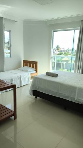 two beds in a white room with a window at Barra de Jacuípe - Condomínio Parque Jacuípe -Mansão Caldeira in Camaçari