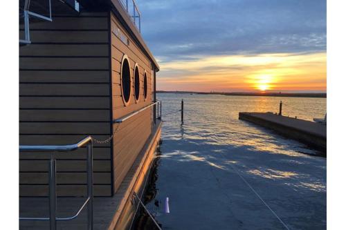 un edificio junto a un cuerpo de agua con la puesta de sol en Hausboot Fjord Cumulus Solarboot mit Biosauna in Wendtorf, en Wendtorf
