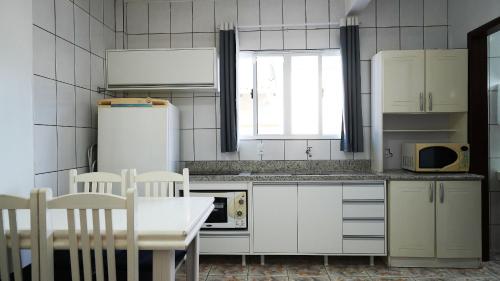 a kitchen with white appliances and a table and chairs at Residencial Adolfo - Mestre Naro in Bombinhas