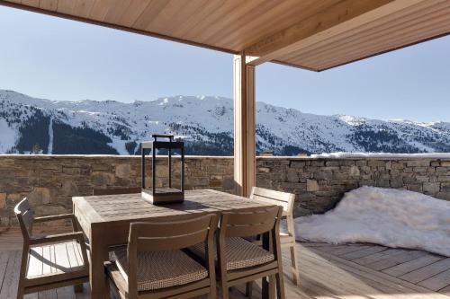 une table et des chaises en bois sur une terrasse avec des montagnes enneigées dans l'établissement Antarès STELLA 001 - Ski inski out apartment, à Méribel