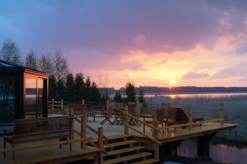 a dock with benches and a house with the sunset at Hotel Joseph Conrad SPA & Wellness in Pisz