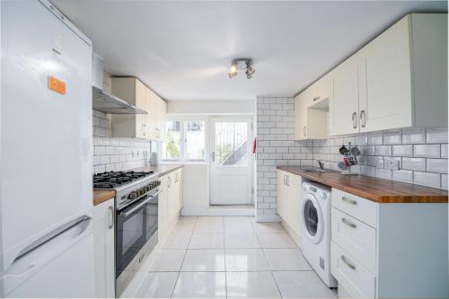 a kitchen with white cabinets and a washer and dryer at Beautiful House Refurbished in London