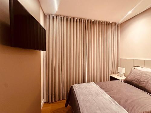 a bedroom with a bed and a window with curtains at Apartamento frente Av Osvaldo Aranha Centro Canela in Canela