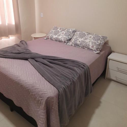 a bed with a purple blanket and a pillow at Apartamento praia do quilombo Centro - 02 in Penha