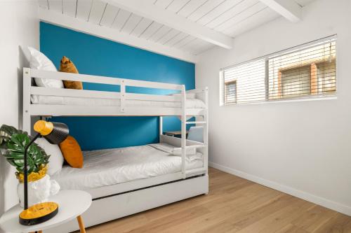 a bedroom with white bunk beds and a blue accent wall at NEW! Ocean View Mid-Century Modern Beach House in Manhattan Beach