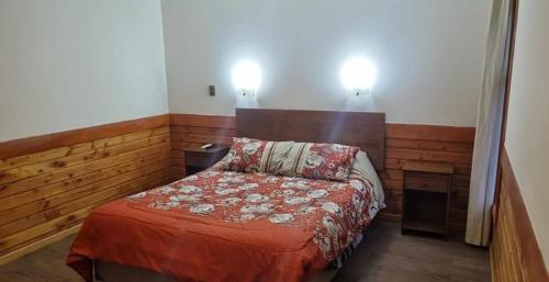 a small bedroom with a bed and two lights on the wall at Cabañas Vista Rio in Puerto Aisén