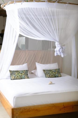 a bed with a canopy with white curtains and pillows at Infinity Beach Boutique Hotel & SPA in Matemwe