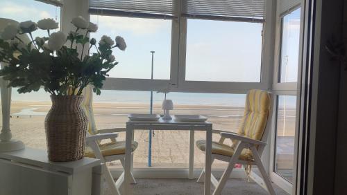 a table and chairs with a vase of flowers in a room at Vue Panoramique FACE MER in Bray-Dunes
