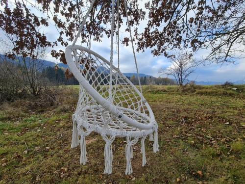 a white chair hanging from a tree in a field at Wataha pod Basztami - Wadera - Domki całoroczne in Wünschelburg